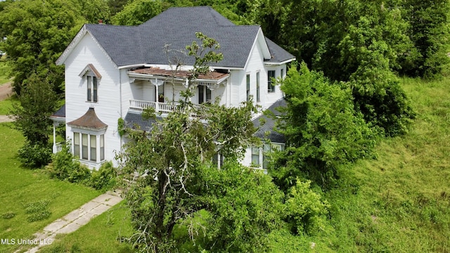 victorian-style house with a balcony, roof with shingles, and a front lawn