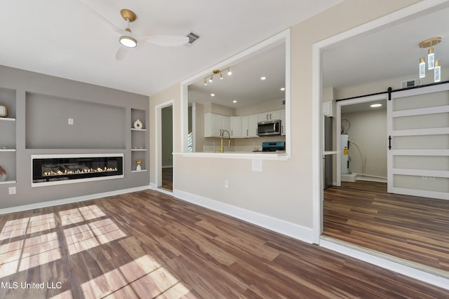 unfurnished living room with water heater, wood-type flooring, a barn door, built in features, and ceiling fan