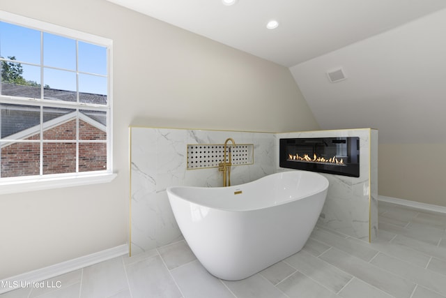 bathroom featuring tile walls, vaulted ceiling, a bathtub, and a wealth of natural light