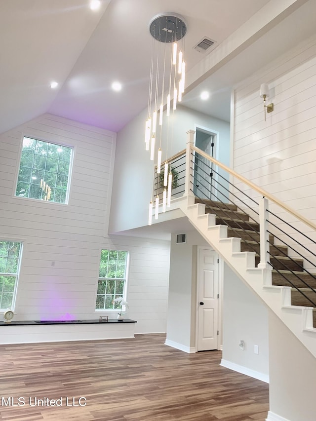 stairs featuring high vaulted ceiling, wooden walls, and hardwood / wood-style floors