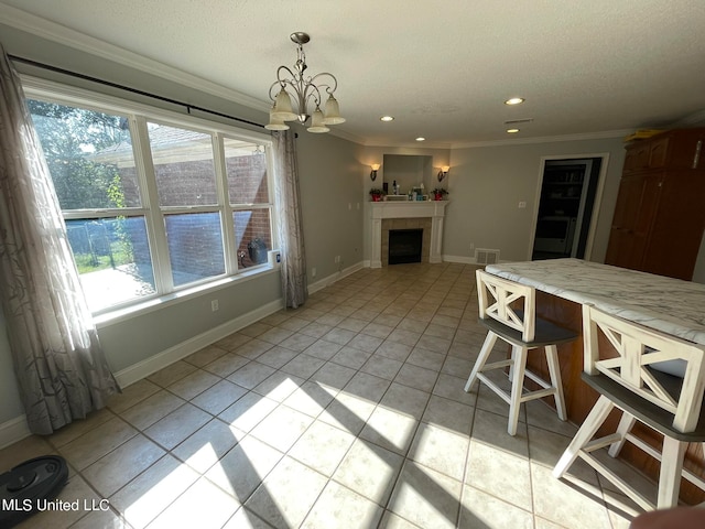 kitchen featuring light tile patterned flooring, a kitchen bar, hanging light fixtures, ornamental molding, and a tiled fireplace