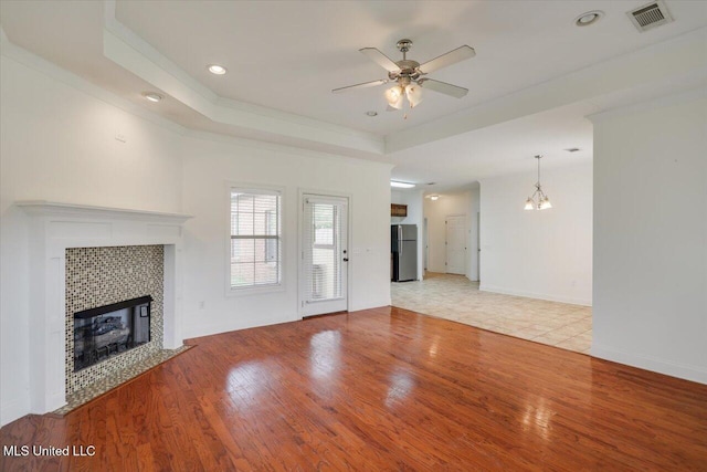 409 Sand Stone Pl, Brandon, MS 39042 - unfurnished living room with a tray ceiling, ceiling fan, a tiled fireplace, light wood finished floors, and a chandelier