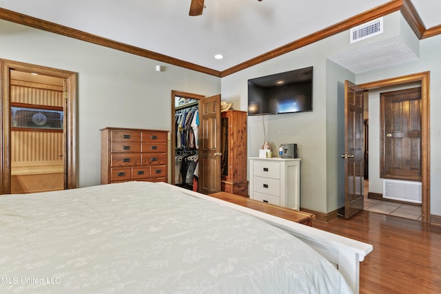 bedroom with hardwood / wood-style flooring, a closet, a spacious closet, ornamental molding, and ceiling fan