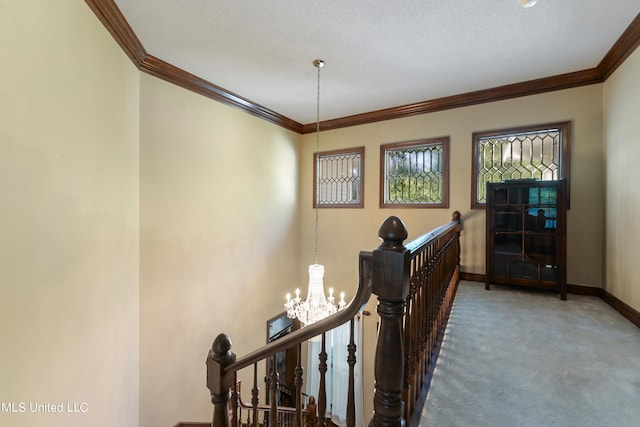 hallway featuring an inviting chandelier, ornamental molding, a textured ceiling, and carpet