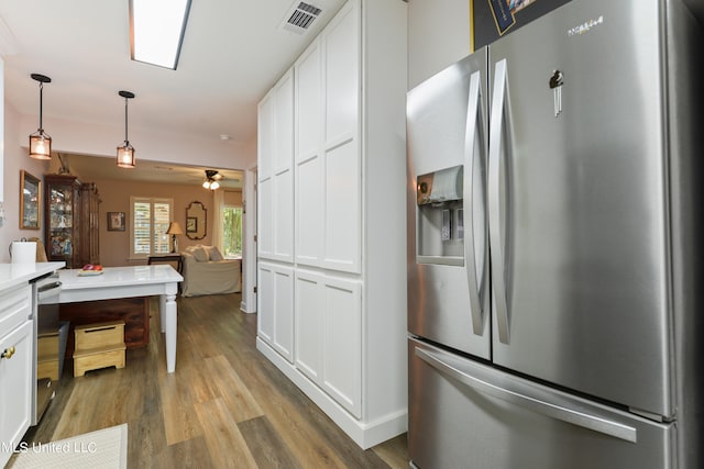 kitchen with built in desk, stainless steel fridge with ice dispenser, white cabinetry, light hardwood / wood-style flooring, and pendant lighting