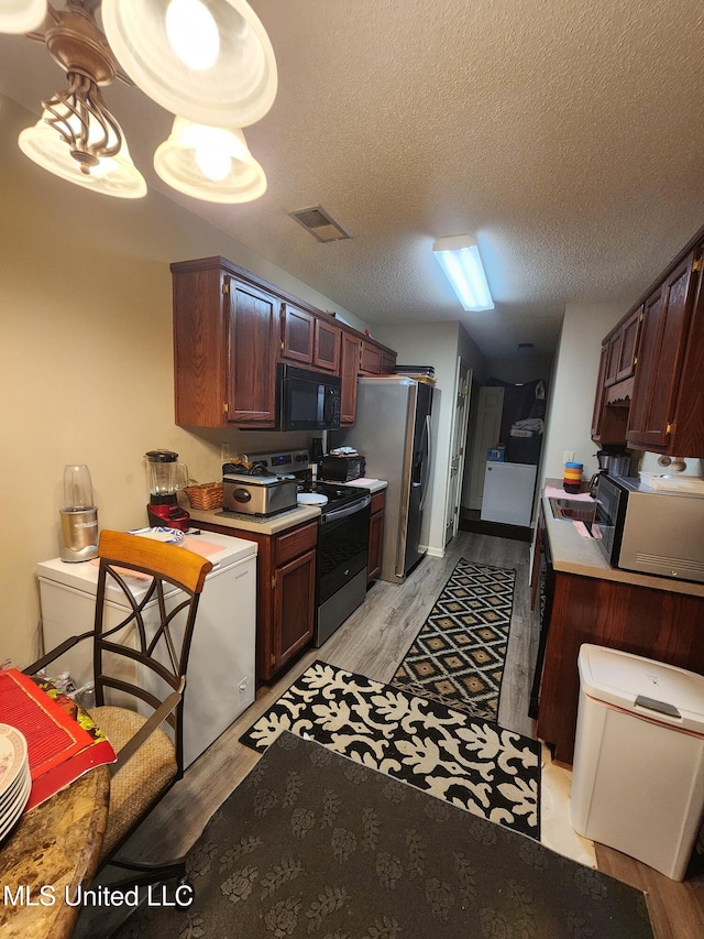 7295 Madelyn Cv, Horn Lake, MS 38637 - kitchen featuring electric range, black microwave, stainless steel fridge, light wood-type flooring, and a textured ceiling