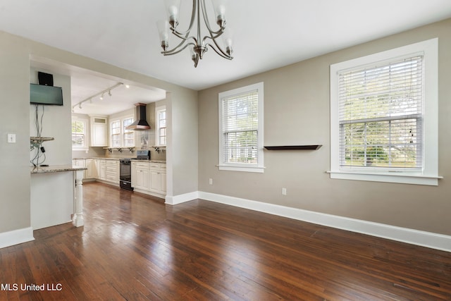 interior space with an inviting chandelier, rail lighting, a wealth of natural light, and dark hardwood / wood-style flooring