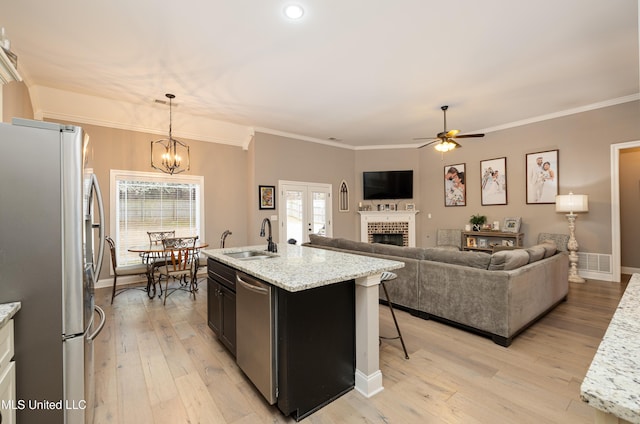 kitchen with sink, a kitchen island with sink, stainless steel appliances, a brick fireplace, and decorative light fixtures