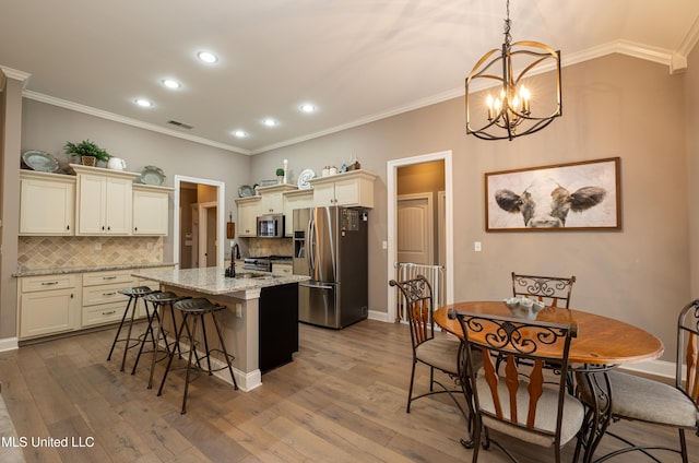 kitchen featuring stainless steel appliances, cream cabinetry, light stone counters, and decorative light fixtures