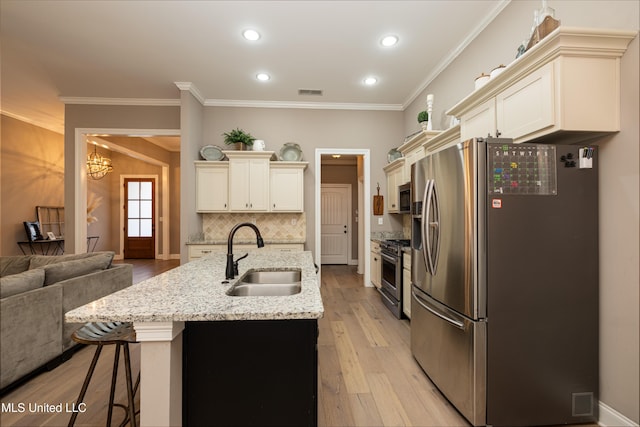 kitchen with sink, a breakfast bar area, appliances with stainless steel finishes, a kitchen island with sink, and cream cabinetry