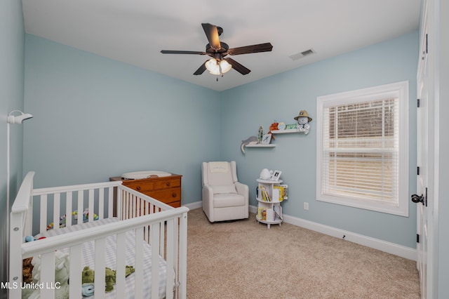 bedroom with a crib, light colored carpet, and ceiling fan