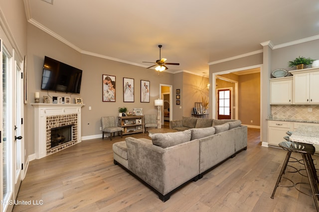 living room featuring crown molding, a brick fireplace, ceiling fan, and light hardwood / wood-style flooring