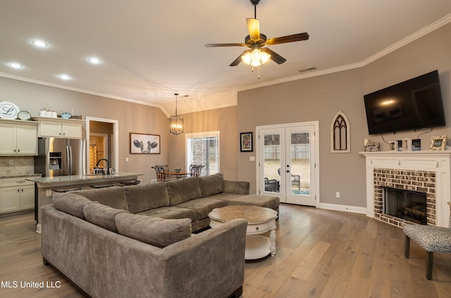 living room featuring crown molding, a fireplace, french doors, and light wood-type flooring