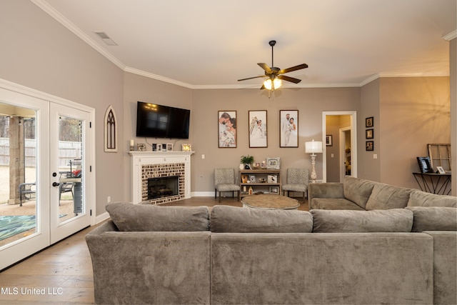 living room featuring french doors, ornamental molding, ceiling fan, a fireplace, and light hardwood / wood-style floors