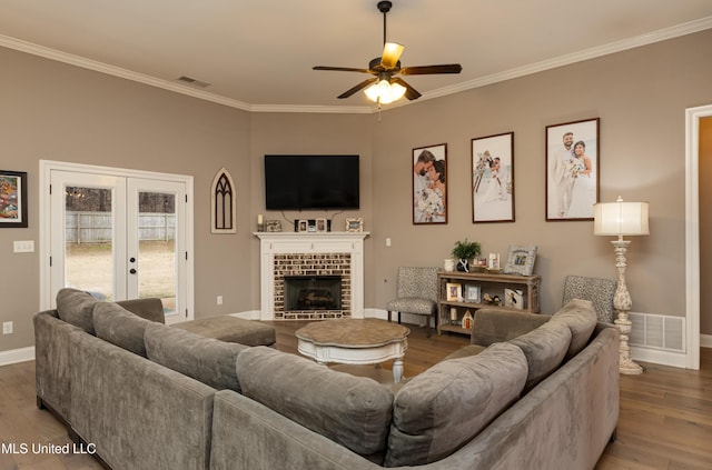 living room with french doors, wood-type flooring, ornamental molding, ceiling fan, and a fireplace