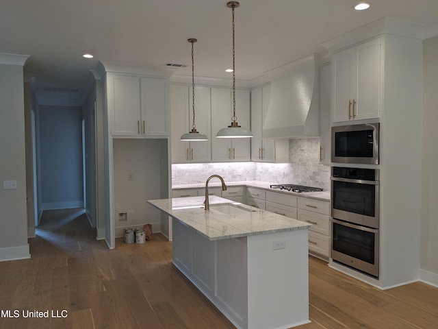 kitchen featuring appliances with stainless steel finishes, sink, light stone counters, hardwood / wood-style flooring, and a kitchen island with sink