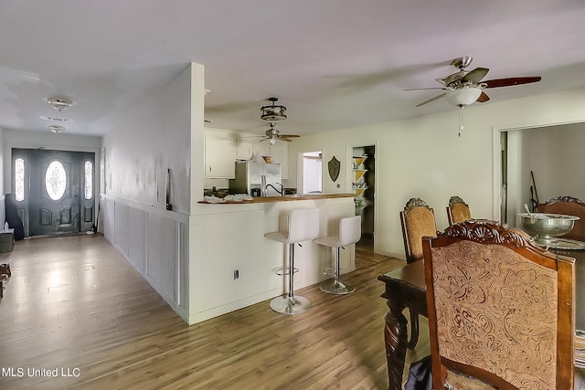 kitchen with kitchen peninsula, stainless steel fridge with ice dispenser, a breakfast bar, white cabinetry, and hardwood / wood-style flooring