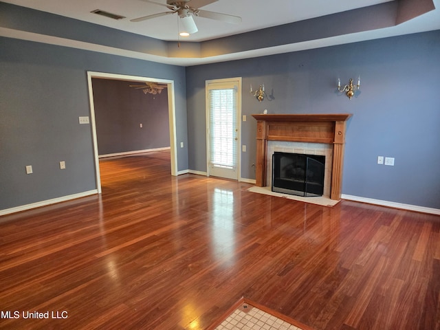 unfurnished living room featuring a tray ceiling, a tiled fireplace, ceiling fan, and hardwood / wood-style floors