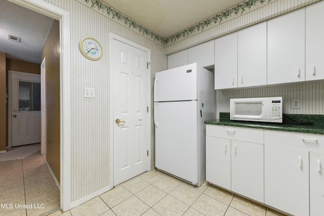 kitchen featuring white appliances, a textured ceiling, white cabinetry, and light tile patterned flooring