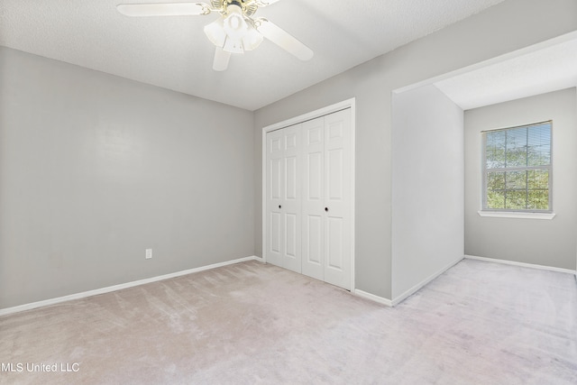 unfurnished bedroom with a textured ceiling, light colored carpet, a closet, and ceiling fan