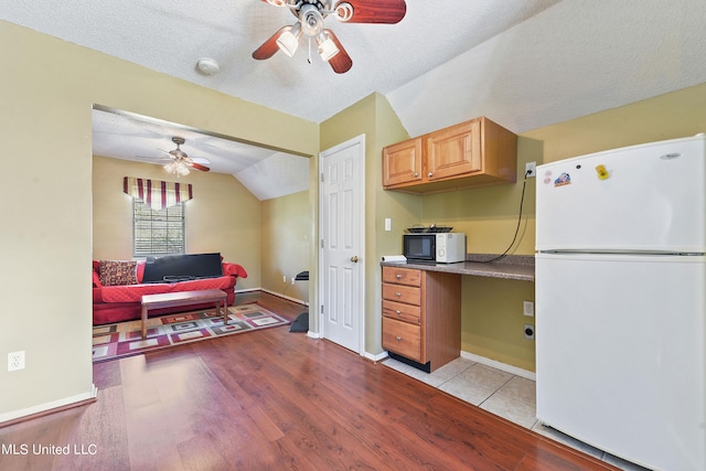 kitchen featuring white appliances, light wood-type flooring, built in desk, a textured ceiling, and lofted ceiling