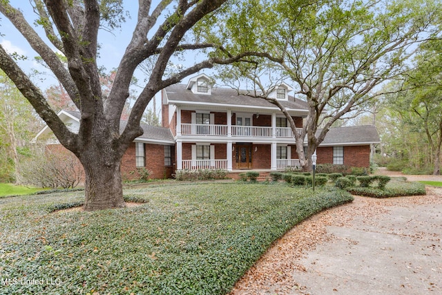 greek revival inspired property with covered porch, a balcony, and a front lawn