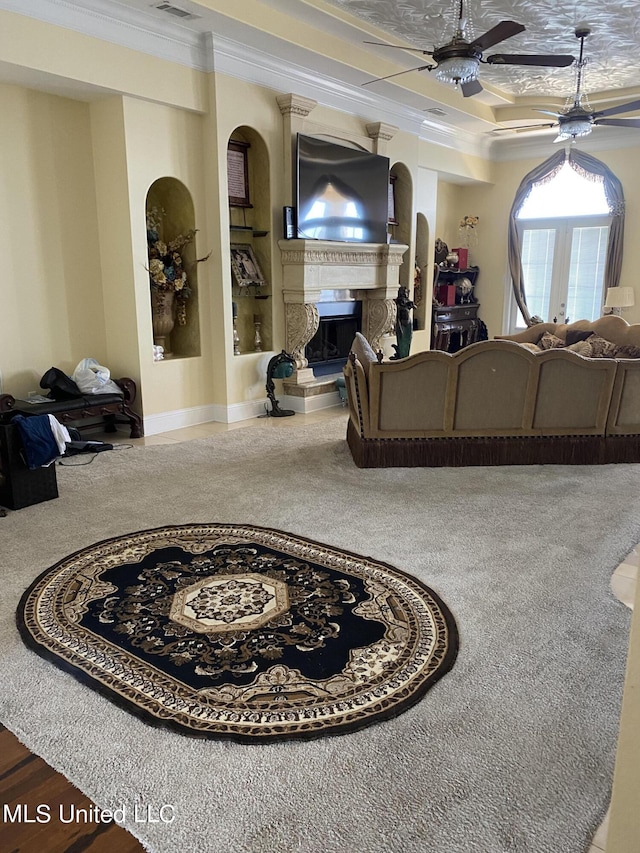 living area featuring crown molding, a fireplace with raised hearth, ceiling fan, carpet floors, and visible vents