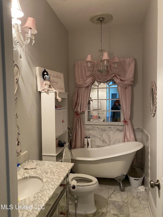 full bath with toilet, a notable chandelier, a freestanding tub, marble finish floor, and vanity