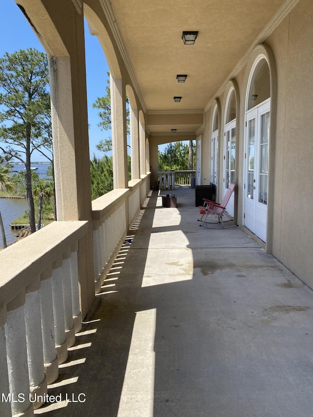 view of patio featuring french doors, a water view, and a balcony