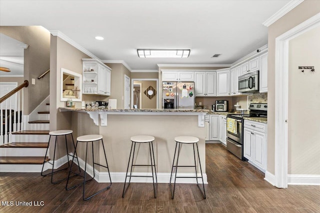 kitchen with dark wood-style floors, a breakfast bar area, appliances with stainless steel finishes, a peninsula, and crown molding