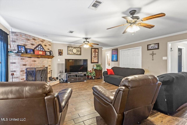 living room with a brick fireplace, visible vents, crown molding, and wood finished floors