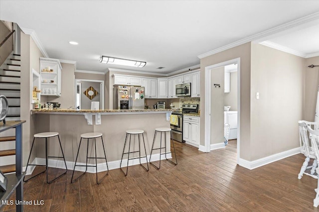 kitchen with appliances with stainless steel finishes, white cabinets, wood finished floors, a peninsula, and a kitchen bar