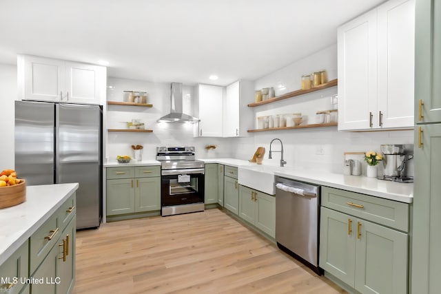 kitchen with appliances with stainless steel finishes, tasteful backsplash, wall chimney exhaust hood, sink, and light hardwood / wood-style flooring