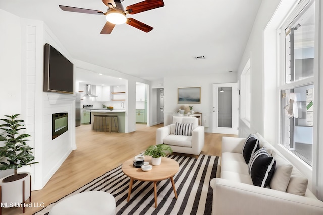 living room featuring ceiling fan, light wood-type flooring, and a fireplace