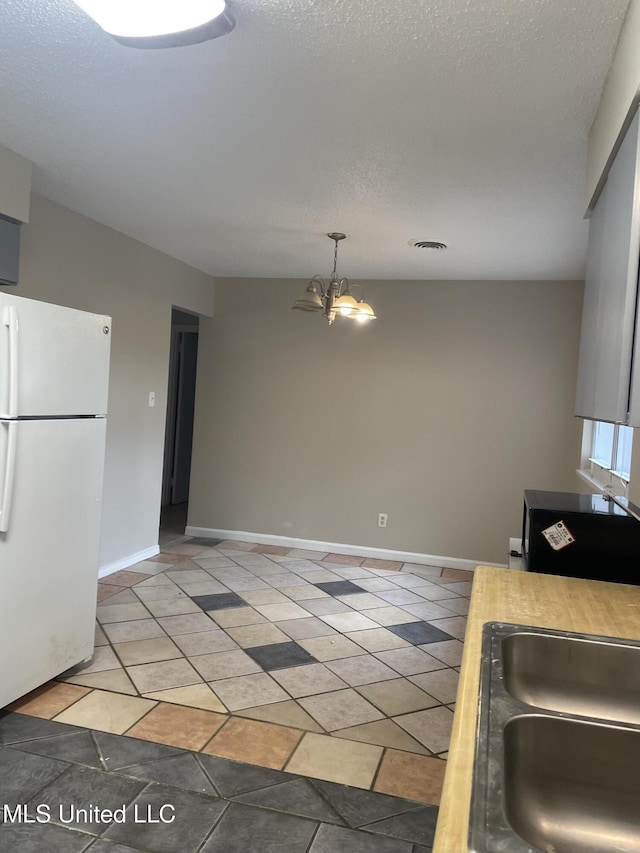 kitchen featuring white fridge, a notable chandelier, a textured ceiling, and decorative light fixtures