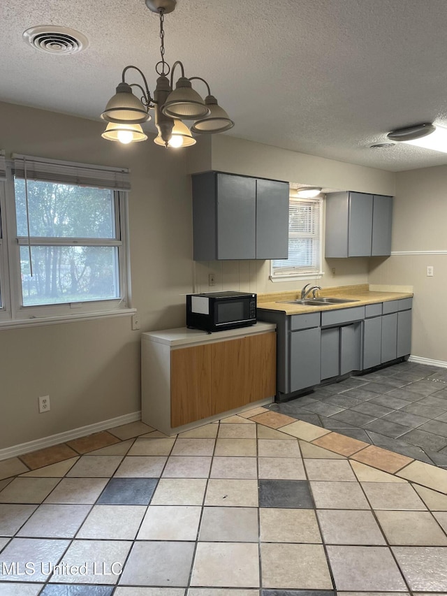 kitchen with gray cabinets, light tile patterned flooring, pendant lighting, sink, and a textured ceiling