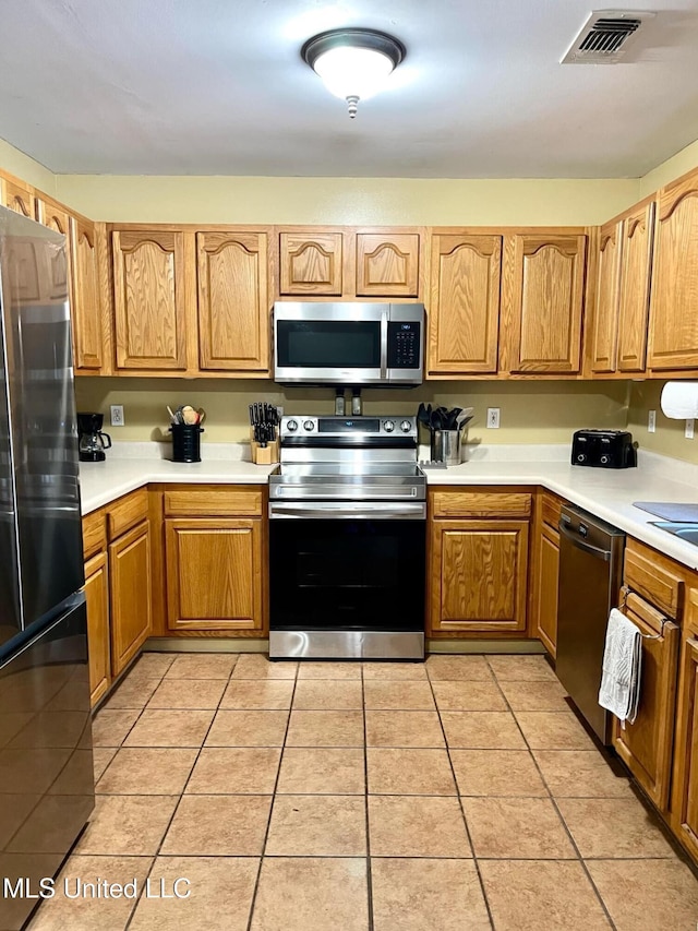 kitchen featuring light tile patterned floors, stainless steel appliances, visible vents, light countertops, and brown cabinets