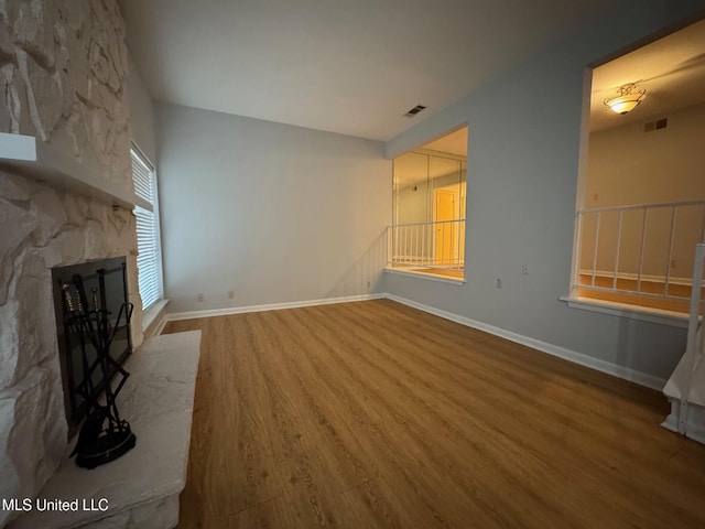 unfurnished living room featuring visible vents, baseboards, wood finished floors, and a stone fireplace