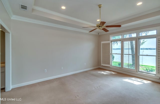 carpeted empty room with a water view, ceiling fan, a raised ceiling, and ornamental molding