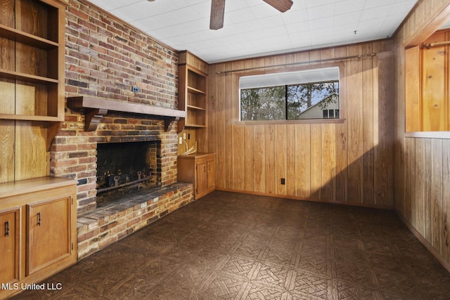 unfurnished living room with ceiling fan, a fireplace, wooden walls, and built in shelves