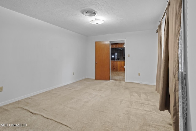 spare room featuring light colored carpet and a textured ceiling