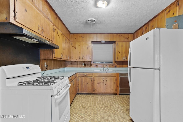 kitchen featuring sink, white appliances, wooden walls, and a textured ceiling