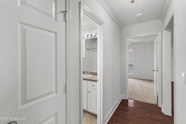 hallway with baseboards, wood finished floors, a sink, and crown molding