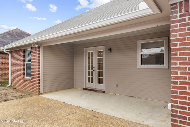 property entrance with brick siding, roof with shingles, and a patio area