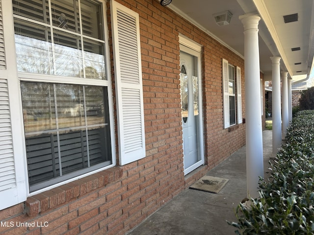 doorway to property featuring covered porch, visible vents, and brick siding