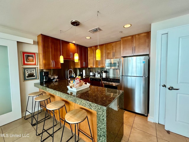 kitchen with light tile patterned flooring, kitchen peninsula, a kitchen breakfast bar, stainless steel appliances, and decorative light fixtures