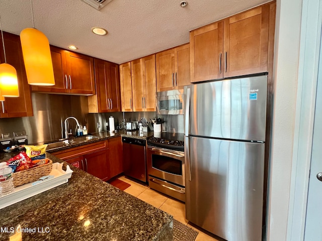 kitchen with dark stone counters, sink, pendant lighting, light tile patterned floors, and appliances with stainless steel finishes