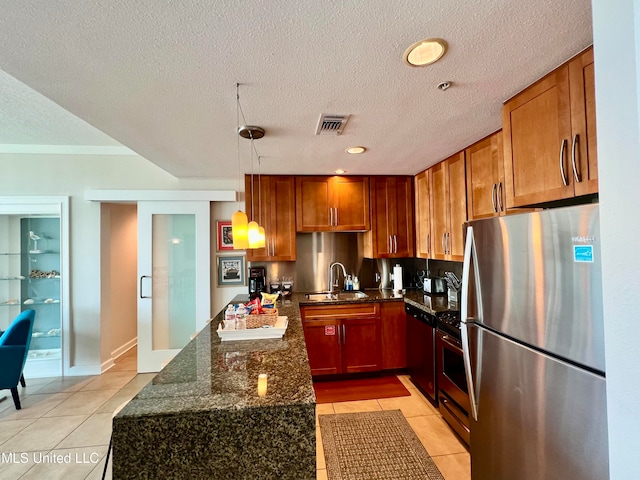 kitchen featuring light tile patterned floors, appliances with stainless steel finishes, a textured ceiling, dark stone countertops, and pendant lighting