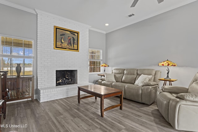 living room with a brick fireplace, crown molding, and wood finished floors