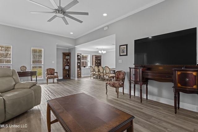 living area featuring ornamental molding, ceiling fan with notable chandelier, baseboards, and wood finished floors